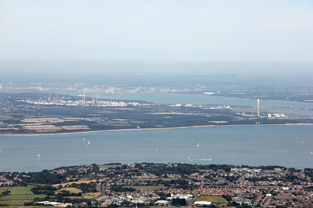 From above West Cowes looking north over the Solent: the many tall chimney stacks of Fawley Oil Refinery are evident left of centre, 
				with Southampton visible beyond it at the end of Southampton Water, and Calshot Tower to the right.